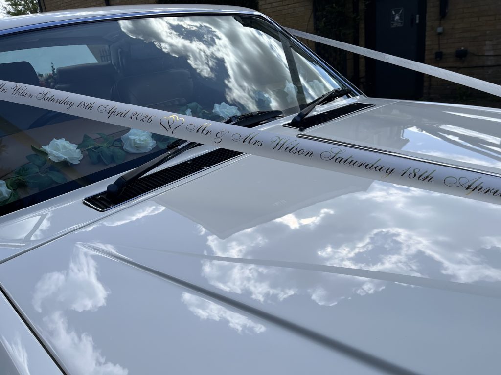 Wedding car bonnet detail with personalised ribbon and floral decoration on classic Rolls-Royce