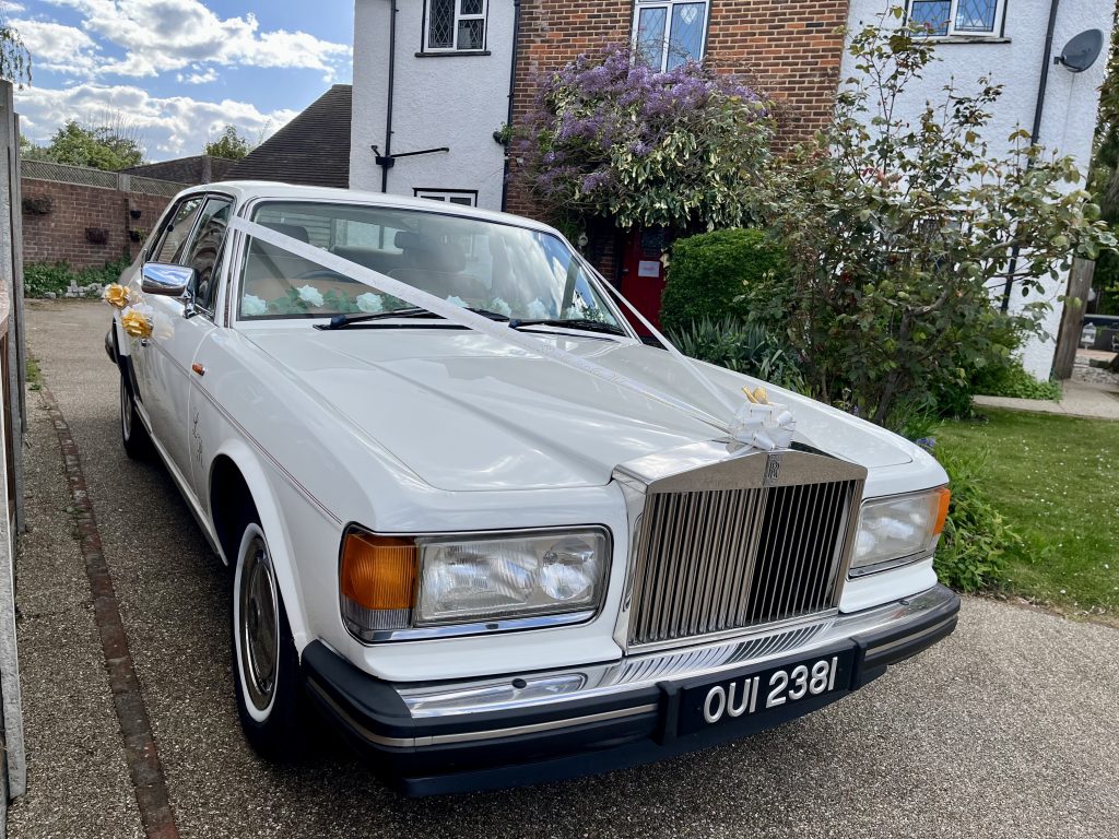 Classic white Rolls-Royce wedding car decorated with ribbons parked ready for a wedding day
