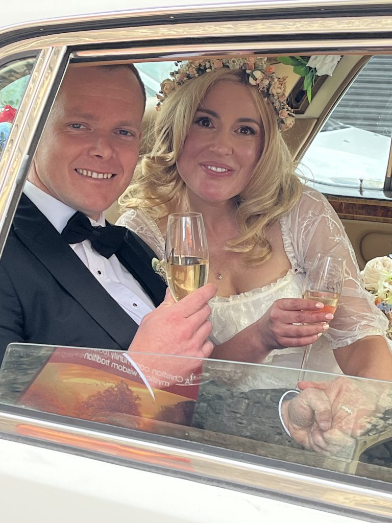 Newlywed couple inside classic Rolls-Royce wedding car toasting with champagne